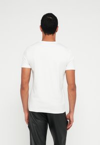 Biała koszulka z krótkim rękawem wykonana z bawełny, z okrągłym dekoltem, w gładkim wzorze i regularnym krojem, noszona z czarnymi spodniami.