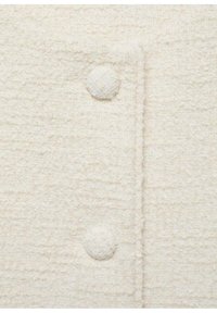 Biała tkanina o teksturowanej, miękkiej, tkanej powierzchni. Posiada wąski listek oraz okrągły, ozdobny guzik po lewej stronie.