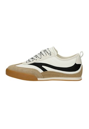 Bílé a béžové nízké tenisky s černým postranním pruhem, vzorovanými tkaničkami a gumovou podrážkou, zobrazené v bočním profilu na bílém pozadí.