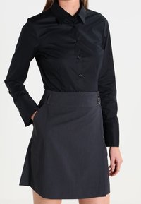 Svart långärmad skjorta med knappar som matchas med en mörkgrå kjol med skräddarsydd passform, sidoficka och två dekorativa knappar vid midjan.