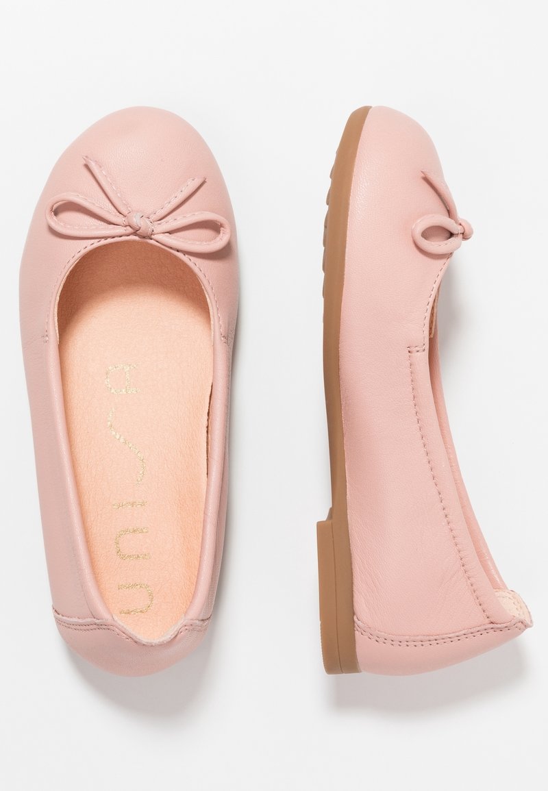 Paire de ballerines en cuir rose avec petits nœuds à l'avant et semelles en caoutchouc marron clair, vues de dessus et de côté.