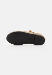 Sandal plana con una parte superior tejida en oro, lazo decorativo y una suela de goma negra. Presenta un acabado texturizado y una forma contorneada.