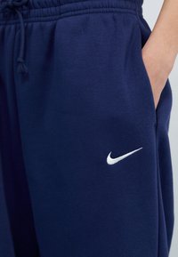 Tumed sinised dressipüksid pehmest kangast, elastse vöökoha ja nööriga, vasakul jalal valge Nike logo.