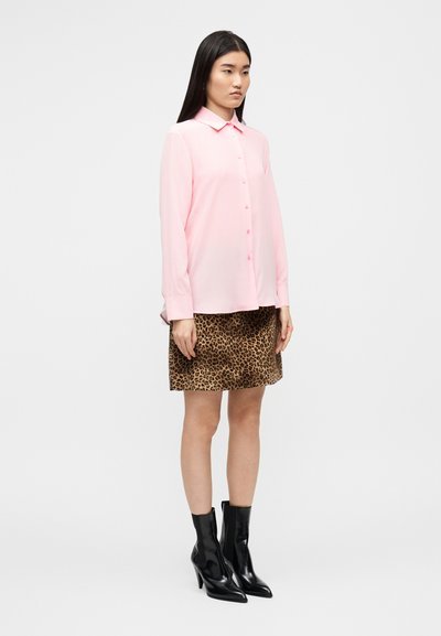 Ροζ μπλούζα με μακριά μανίκια και κουμπιά, συνδυασμένη με φούστα με λεοπάρ σχέδιο και μαύρα μποτάκια με τακούνι. Λείο ύφασμα και εφαρμοστή γραμμή.