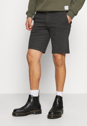 Pantaloni corti grigio carbone realizzati in materiale morbido con fronte piatto, abbinati a stivali neri alla caviglia con cuciture gialle e pannelli elasticizzati laterali.