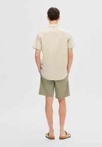 Kortermet beige skjorte med krage, kombinert med olivengrønne shorts og beige sandaler. Enkelt design, lett stoff, avslappet passform.