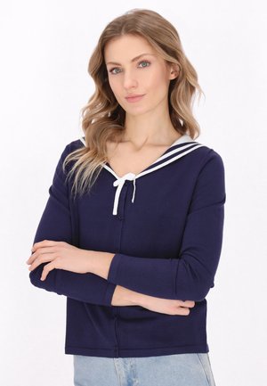 Marineblauwe cardigan met witte zeilercollage, voorzien van een striksluiting en een knopenrij aan de voorkant. Lange mouwen, lichtgewicht stof en een getailleerde pasvorm.