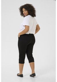 Black cropped trousers with a sleek, fitted design and back pockets, paired with a loose white t-shirt and flat black shoes.