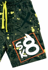 Grønne shorts lavet af stof med sorte og gule graffiti-mønstre, med en lys gul snor og et fremtrædende hvidt og orange logo.