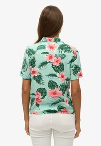 Camicia a maniche corte verde menta con motivo floreale di ibischi rosa e foglie verdi. Tessuto liscio, colletto classico, vestibilità comoda.