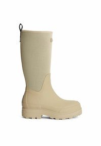 Beige kumisaappaat, jotka ovat vedenpitävät ja niissä on teksturoitu, saumaton päällinen, kestävä pohja sekä takana vetoketju helppoa pukemista varten.