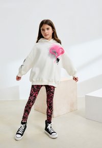 Oversized white hoodie with pink flamingo graphic, paired with black leggings featuring a pink abstract pattern, and black high-top sneakers.