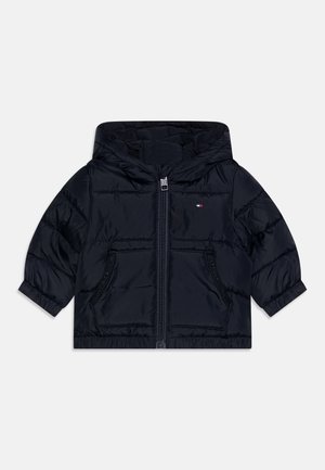 Veste matelassée à capuche bleu marine avec fermeture éclair à l'avant, deux poches zippées, poignets élastiques et petit logo brodé sur le côté gauche de la poitrine.