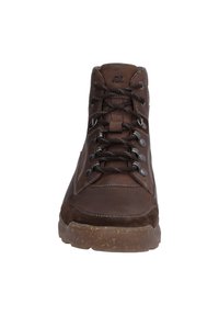 Zapato alto de cuero marrón con acentos de ante, ojales de metal y costuras en contraste sobre una suela de goma texturizada.