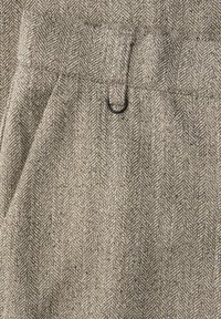 Heringbone-Musterstoff in Beige- und Grautönen mit subtiler Textur; verfügt über einen schwarzen Metallring als Akzent am Bund.