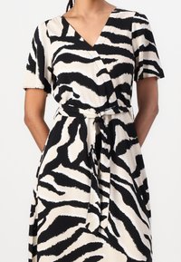 Wrap šaty se zebrovaným potiskem v černobílé barvě, krátkými rukávy, výstřihem do V, s páskem na zavázání a hladkým, lehkým materiálem.
