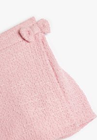 Hellrosa Handtuch mit strukturierter Webart, das an einem Ende mit einer kleinen, gestrickten Schleife verziert ist. Weiches, saugfähiges Material mit einem leicht geschlungenen Muster.