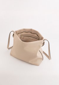 Beżowa torba ze sk�órki w fakturze, o miękkim, nieusystematyzowanym kształcie. Posiada wewnętrzną kieszeń na zamek oraz kontrastowe czarne wykończenie wzdłuż krawędzi.