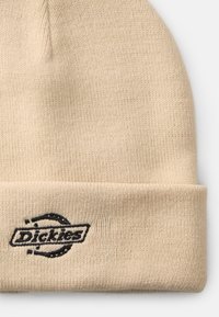 Gorro de malha bege com um logótipo preto bordado "Dickies" na bainha, apresentando um tecido texturizado e elástico e um topo arredondado.