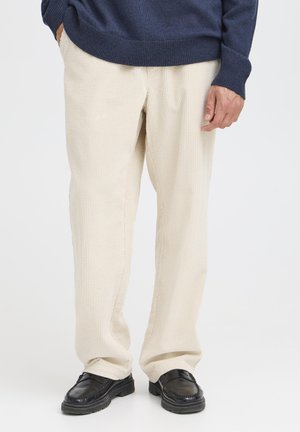 Beige kordfløyelbukser med ribbet tekstur, rett ben design, kombinert med svarte skinnsko og en marineblå genser.