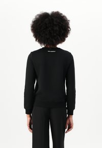 Svart hettegenser med rund hals og ribbede mansjetter. På baksiden vises "KARL LAGERFELD"-logoen i hvitt over halsen.
