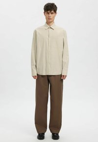 Ruuduline pikkade varrukatega särk helebeeži ja pruuni toonis; sellel on klassikaline krae, ees nööbid ja lahtine lõige, mida on kombineeritud pruunide pükstega.