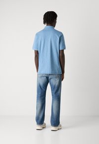 Camisa polo de manga curta azul clara com uma textura suave, usada com jeans retos azuis desgastados. Apresenta um colarinho clássico e sem logótipos visíveis.