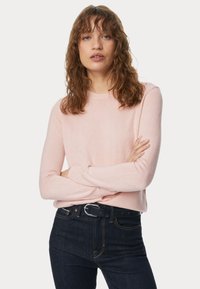 Maglione rosa chiaro con maniche lunghe, scollatura rotonda e una consistenza morbida, abbinato a jeans in denim scuro e una cintura nera con fibbia argentata.