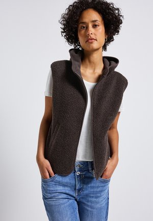 Gilet en polaire marron foncé avec une surface douce et texturée, doté d'une capuche, d'une fermeture éclair sur le devant et de deux poches latérales, associé à une chemise blanche.