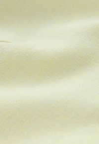 Tissu jaune pâle doux avec une texture tissée subtile et des plis délicats créant une surface lisse et légèrement ondulée.