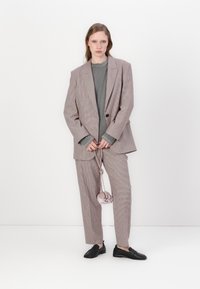 Rutete dress i lys brun og krem, med en dobbeltspent blazer, tettsittende bukser, grå topp under, og svarte sko.