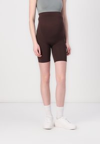 High-waisted, brown shorts made of stretchy material. Smooth texture, knee-length, with a seamless top band and soft fit. Paired with white sneakers.