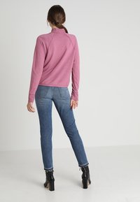 Helles rosa Sweatshirt mit hohem Kragen, kombiniert mit blauen Jeans. Das Outfit besteht aus schwarzen, heeled Stiefeletten und hat eine lässige, entspannte Passform.