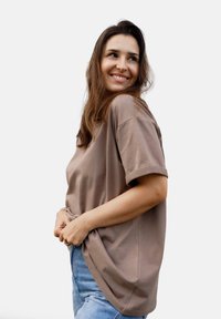 Brązowy oversize'owy t-shirt z krótkimi, podwiniętymi rękawami, wykonany z bawełny, o miękkiej teksturze, stylizowany z jasnoniebieskimi spodniami jeansowymi z wysokim stanem.