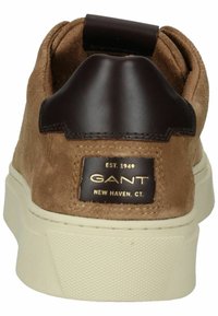 Braune Wildleder-Sneaker mit einem dunkelbraunen Lederakzent an der Ferse, dicke weiße Gummisohle und goldener Logo-Auszeichnung. Glatte Textur mit gestickten Details.