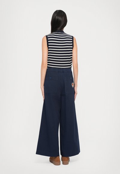 Pantaloni largi de marine cu talie ajustabilă prin cordon, două buzunare la spate și un detaliu cu patch. Asortați cu un top fără mâneci cu dungi navy și albe.