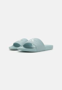 Sandales à glissière bleu clair avec un dessus en tissu texturé, une large bande et une semelle en caoutchouc douce. Le design comprend des détails de logo blancs.