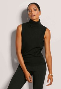 Schwarzes ärmelloses Rollkragenoberteil aus weichem Material, mit taillierter Passform und geripptem Saum, kombiniert mit schwarzen Leggings und einem goldenen Armband.