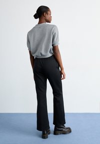 Top cinza de manga curta, calças pretas de cintura elástica e botas pretas chunky. Tecido suave, corte descontraído e design de perna reta.