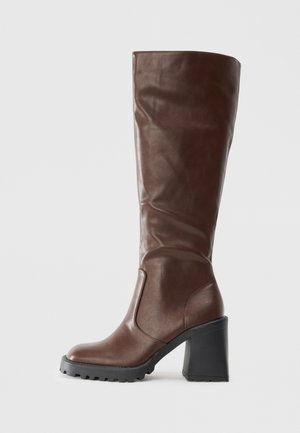 Kõrge tumepruun nahkne saabas paksu musta kanna ja tallaga, külgvaade, sile tekstuur kergete kortsudega varrel.