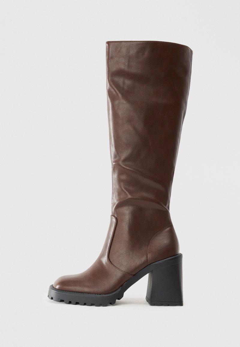Bottine en cuir marron foncé, haute, avec un large talon et une semelle noire, vue de côté, texture lisse avec de légères rides sur la tige.