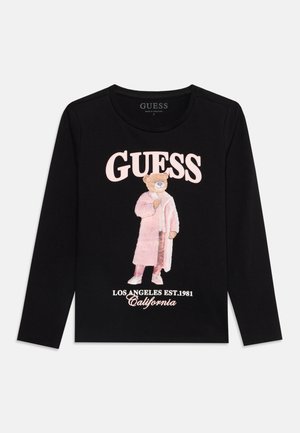 Chemise noire à manches longues avec le texte "GUESS", un ours portant un manteau et un pantalon roses, et "Los Angeles Est. 1981 California" en dessous.