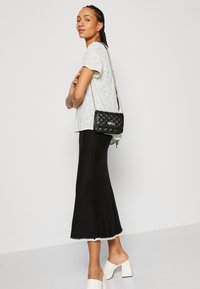 Top bianco a pois neri, gonna nera a campana con orlo scalloped, borsa a tracolla nera trapuntata e mule bianche con tacco a blocco.