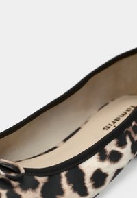 Ballerine à imprimé léopard avec une finition en tissu lisse, un bord noir et un petit nœud décoratif sur le bout. L'intérieur est doublé en beige.