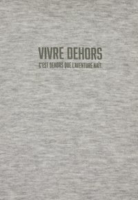 Tissu gris avec texte français en vert foncé indiquant « Vivre dehors » et texte plus petit en dessous : « C’est dehors que l’aventure naît. »