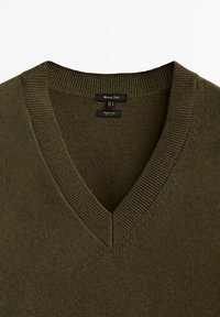 V-hals trui in donker olijfgroen, gemaakt van zacht materiaal met ribbelaccenten bij de halslijn. Labels zichtbaar binnenin de kraag.