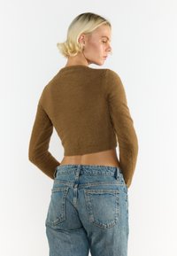 Brauner, verkürzter Pullover aus weich, fuzzy Textur, kombiniert mit hochgeschnittenen hellblauen Denim-Jeans mit Gesäßtaschen und einem leichten Verblassen.