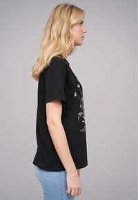 T-shirt en coton noir à manches courtes, avec un imprimé graphique floral blanc sur le devant, à coupe droite et col rond.