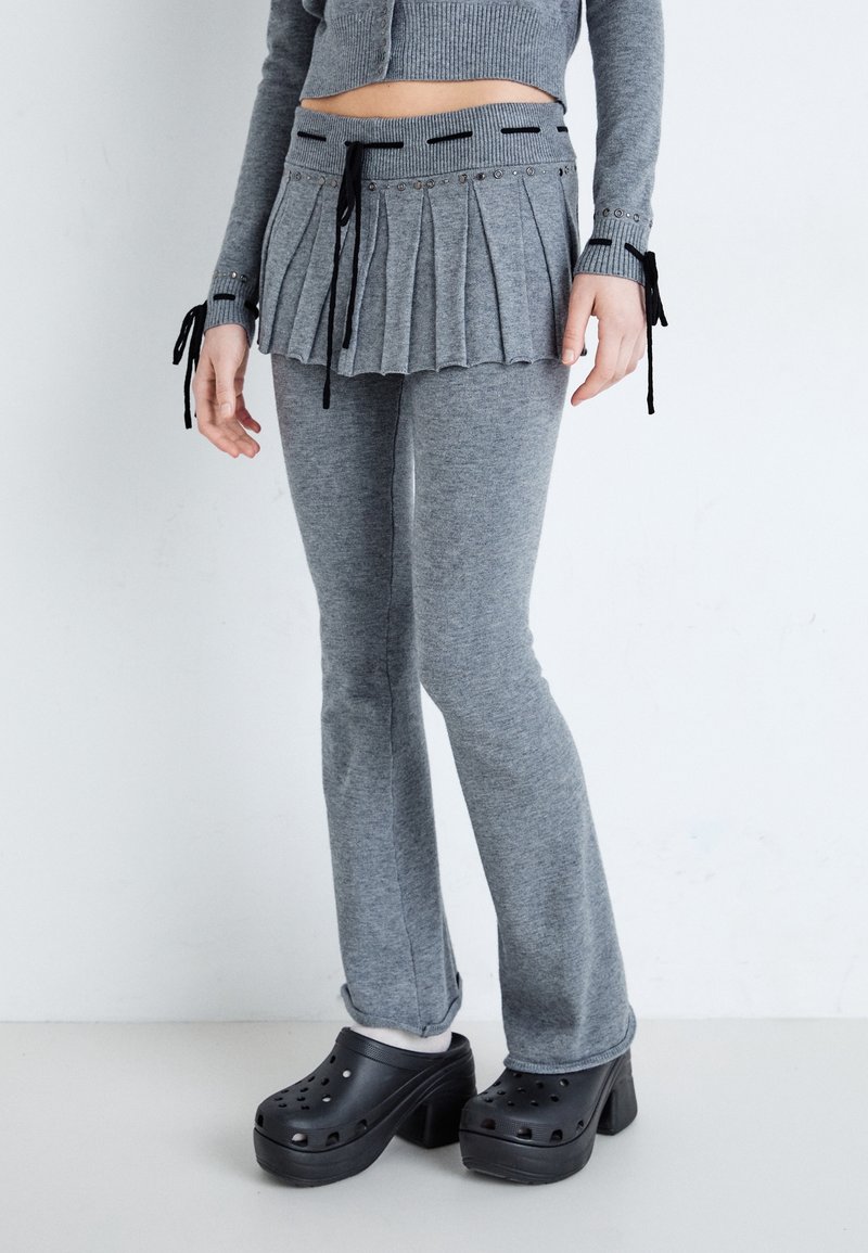 Persona con pantalones de punto grises y una falda plisada superpuesta, suéter corto a juego y zuecos negros de plataforma con calcetines blancos.