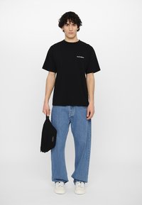 Svart bomull T-skjorte med korte ermer og teksten "No Problemo", parret med lyseblå løstsittende denimjeans og hvite joggesko.